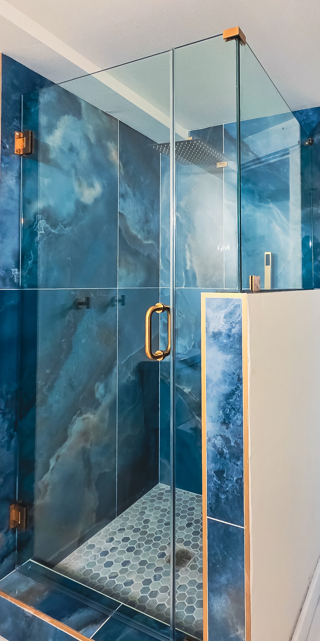 Glass shower enclosure with a hinged door, gold-tone hardware and blue wall tile