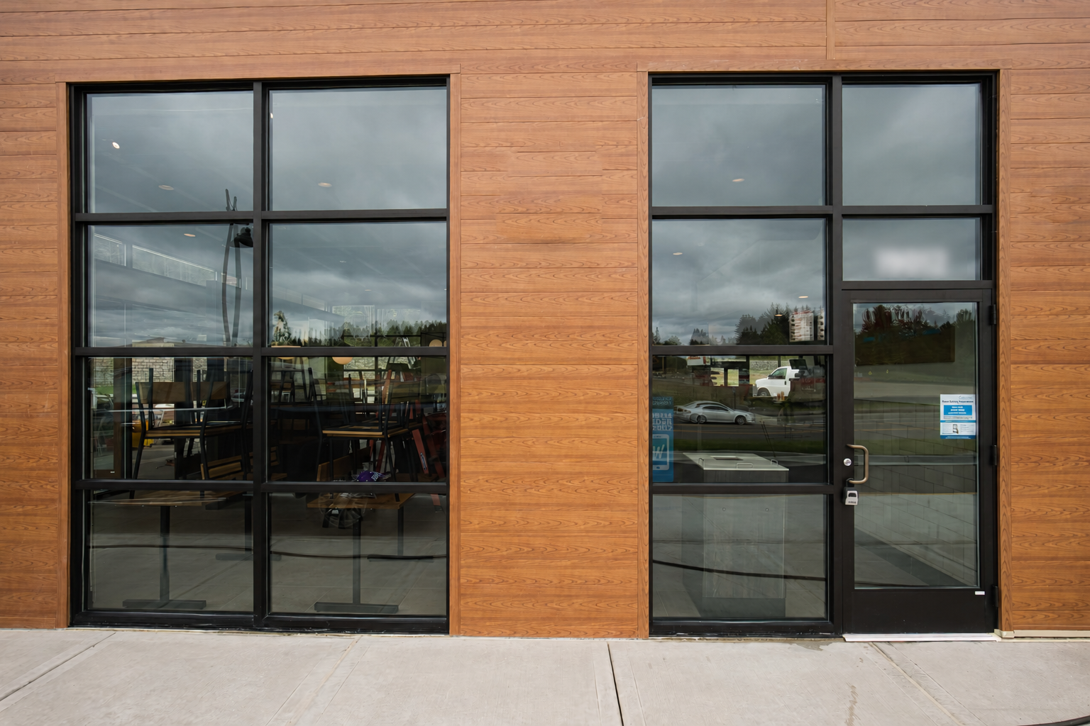 Black-framed storefront windows and entry door beside wood-look exterior cladding